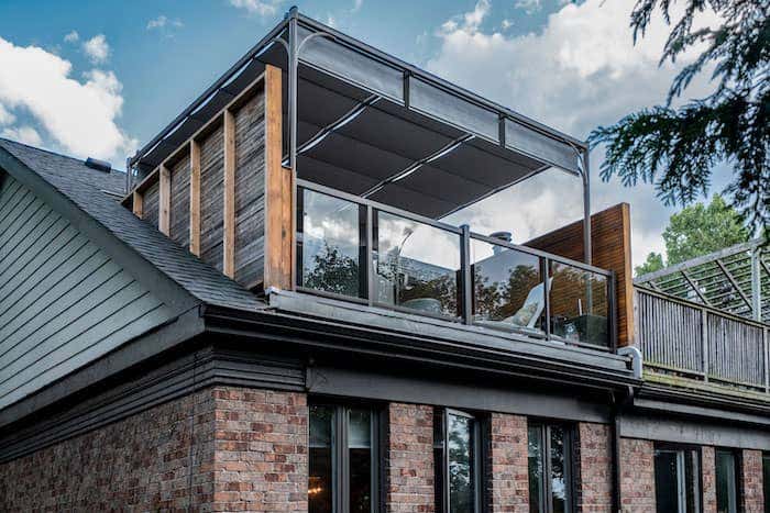 A second story patio outfitted with a bungalow shade structure from ShadeTree clad in a neutral Sunbrella fabric creates the perfect escape to relax and enjoy the view.