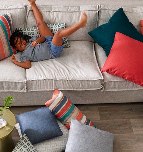 Child playing on a couch with several pillows.