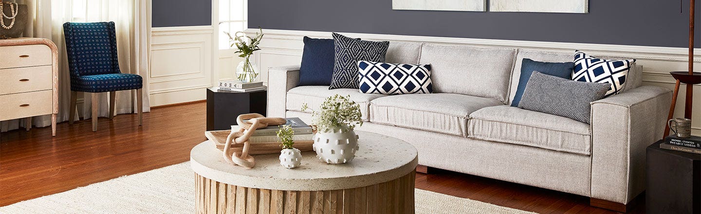 Living room with an eggshell white couch, with blue and grey cushions, and other themed living room furniture in similar colors.