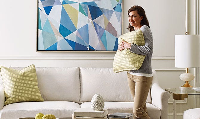 Woman holding a pillow beside a sofa.